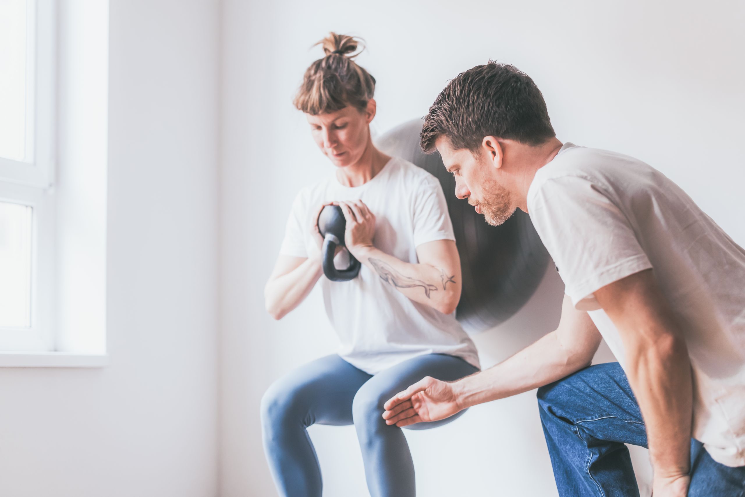 Daniel macht Übungen mit einer Patientin welche in Kniebeugenposition ist und ein Gewicht hebt