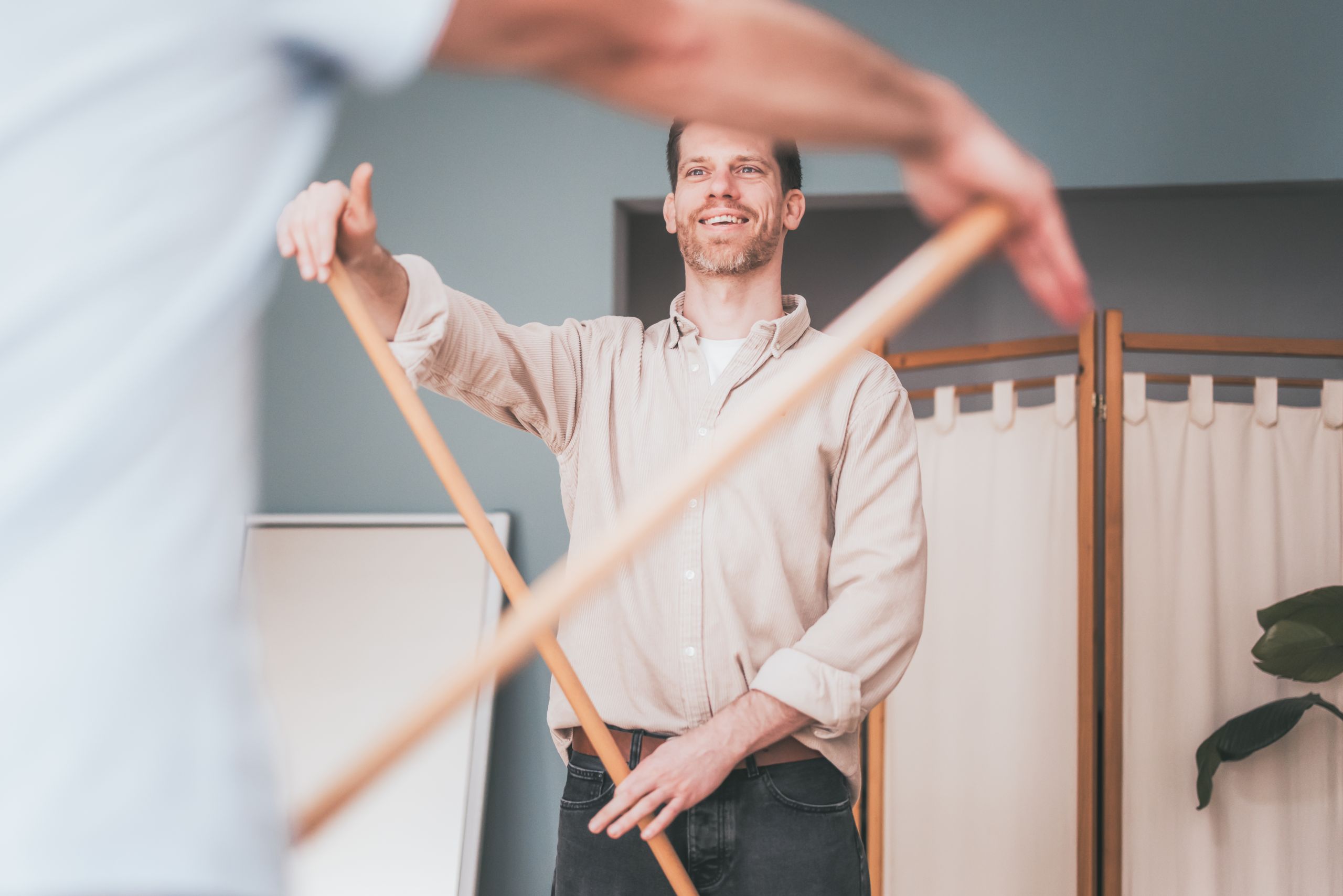 Assistive Schultermobilisation mit einem Stab Daniel macht mit einem Patienten eine Übung mit einem Holzstab
